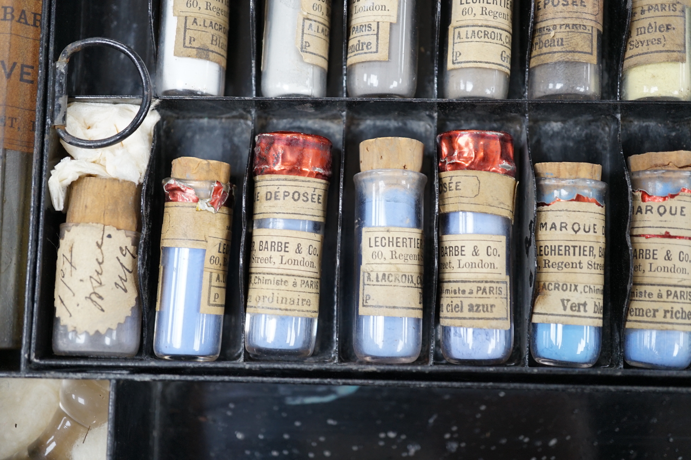 A black artist's tin box, with fitted interior, containing glass phialls of coloured shades of powdered paint and a white glass samples panel etc, box 37.5cm wide, 27cm deep